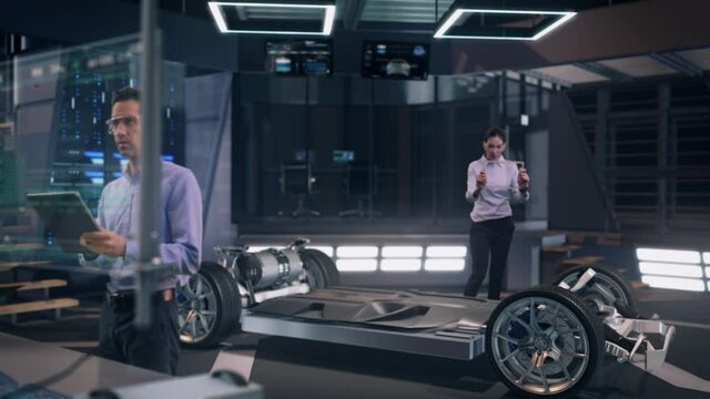 Inside High-Tech Facility: Automotive Professional Engineers working on design of Electric Car using Futuristic Transparent Touchscreen Tablets. Mockup of Electric car chassis.