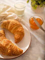 Two croissants, jam and milk on a white tablecloth. Tasty breakfast. Home kitchen. Coffee shop, restaurant, hotel. Cooking, recipes for delicious pastries. Close-up. Careful viewing.