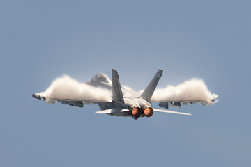 U.S. Navy EA-18G Growler in a high G maneuver, with afterburners on and condensation clouds  over ...