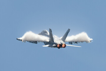 U.S. Navy EA-18G Growler in a high G maneuver, with afterburners on and condensation clouds  over ...