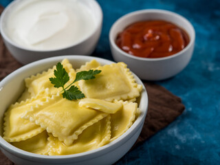 Restaurant and hotel business. Ravioli and two sauces - tomato and sour cream. On top of the ravioli is a mint leaf. White dishes, brown napkin and dark blue background.