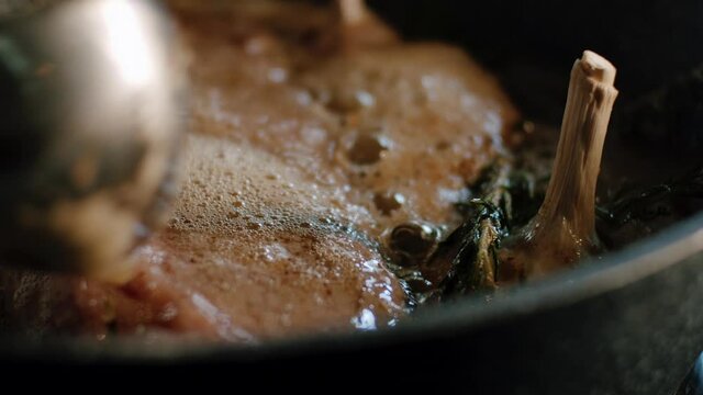 Man is putting melted sizzling butter on piece of meat in hot iron pan, close up