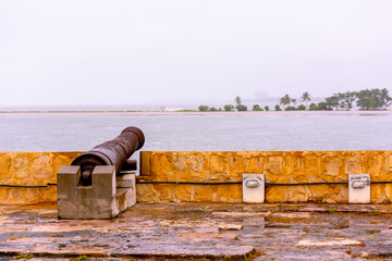 Naklejka premium Cannons of the old fort Orange - Itamaracá - Cloudy sky with a view of the island of Coroa do Avião