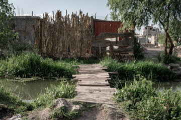 bridge made with pieces of wood in a polluted river near a poor house
