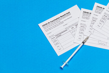 Medical syringe and covid-19 vaccination record cards prepared at healthcare clinic for doctor to...