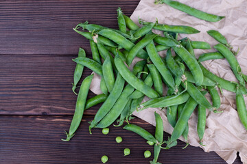 Ripe organic green pea pods on craft paper, close-up, top view.