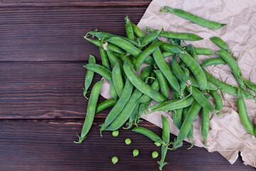 Ripe organic green pea pods on craft paper, close-up, top view.
