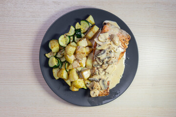 A plate of grilled salmon with mushroom creamy sauce and potato on the side.