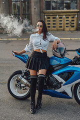 Fototapeta na wymiar Glamour woman biker smoking cigarette leaning bike outside