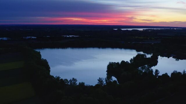 Red glowing sunrise over a calm lake in bavaria, aerial view fyling backward smoothly.