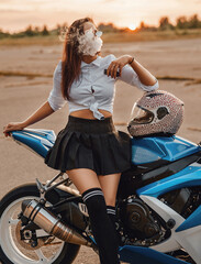 Fototapeta na wymiar Fashionable girl biker smoking vape leaning motorcycle at sunset