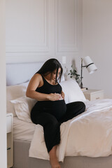 Pregnant Carribbean Indigenous woman practicing self care and putting lotion on baby bump in bed