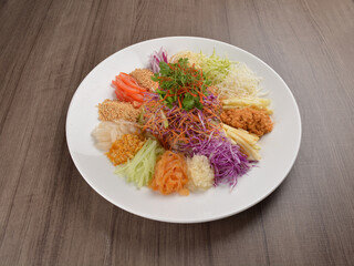 Chinese New Year festival colourful Yu Sheng Lo Hei salad with smoked salmon fish, cracker cookies and sweet sauce on wood background asian halal menu