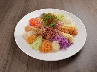 Chinese New Year festival colourful Yu Sheng Lo Hei salad with smoked salmon fish, cracker cookies and sweet sauce on wood background asian halal menu