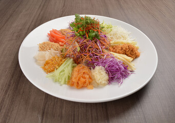 Chinese New Year festival colourful Yu Sheng Lo Hei salad with smoked salmon fish, cracker cookies and sweet sauce on wood background asian halal menu