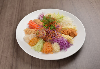 Chinese New Year festival colourful Yu Sheng Lo Hei salad with smoked salmon fish, cracker cookies and sweet sauce on wood background asian halal menu