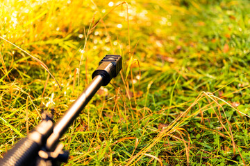 Aiming a rifle in the autumn grass covered with morning dew and sunlit. Close up view from ground level, focus on the flame arrestor