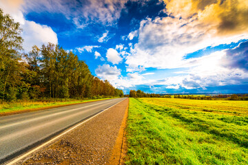 Autumn sky in the clouds lit by the sun over the empty road and boundless fields of the forest. Wide angle view