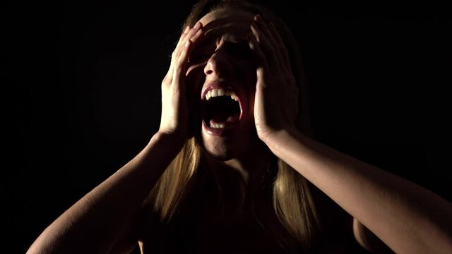 A furious woman expressing her frustration by shouting out loud. A woman in pain screaming in a dramatic way with her mouth wide open and hands touching her head. a woman screaming out of anger.