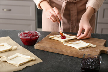Woman filling Danish pastry with fruit jam on kitchen table