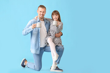 Happy daughter and father with cups of hot cocoa on color background