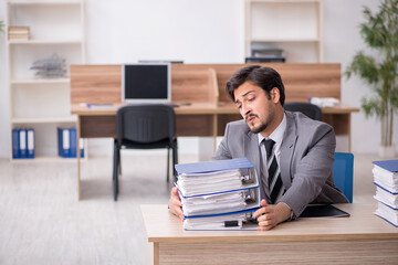 Fototapeta premium Young male employee unhappy with excessive work in the office