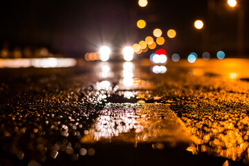 Rainy night in the big city, the car traveling towards the headlights illuminate the road. Close up view from the level of the dividing line