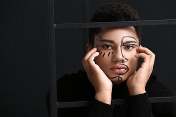 Young African-American guy with paint on face against dark background