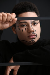 Young African-American guy with paint on face against dark background