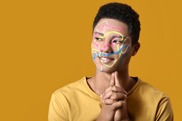 Young African-American guy with paint on face against color background