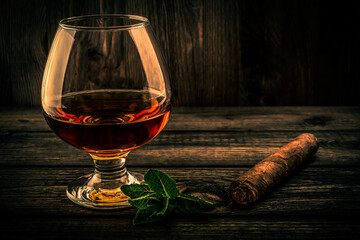 Glass of brandy with mint sprig and cuban cigar on an old wooden table