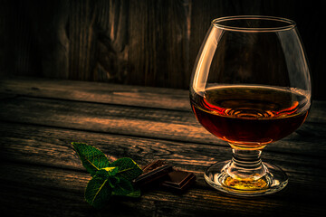 Glass of brandy and a chocolate truffles with mint sprig on an old wooden table. Angle view