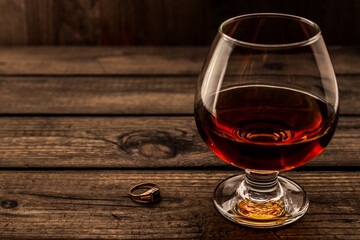 Glass of brandy and golden ring on an old wooden table. Angle view