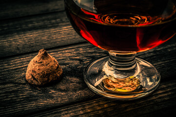 Glass of brandy and a chocolate truffle on an old wooden table. Close up view