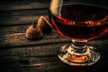 Glass of brandy and a couple of chocolate truffles on an old wooden table. Close up view, shallow depth of field, focus on the chocolate truffles