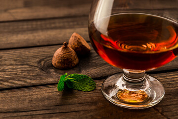 Glass of brandy and a chocolate truffles with mint sprig on an old wooden table. Close up view, shallow depth of field