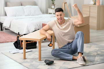 Happy young man assembling furniture at home