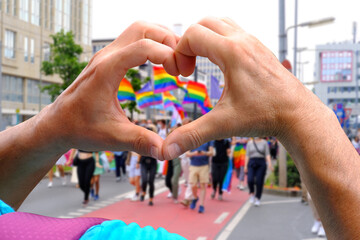 members of LGBTq movement, Gay pride parade in city with rainbow flags, demonstration of people, mass march of lesbian, gay, bisexual, minority festival, male hands close up gesture heart