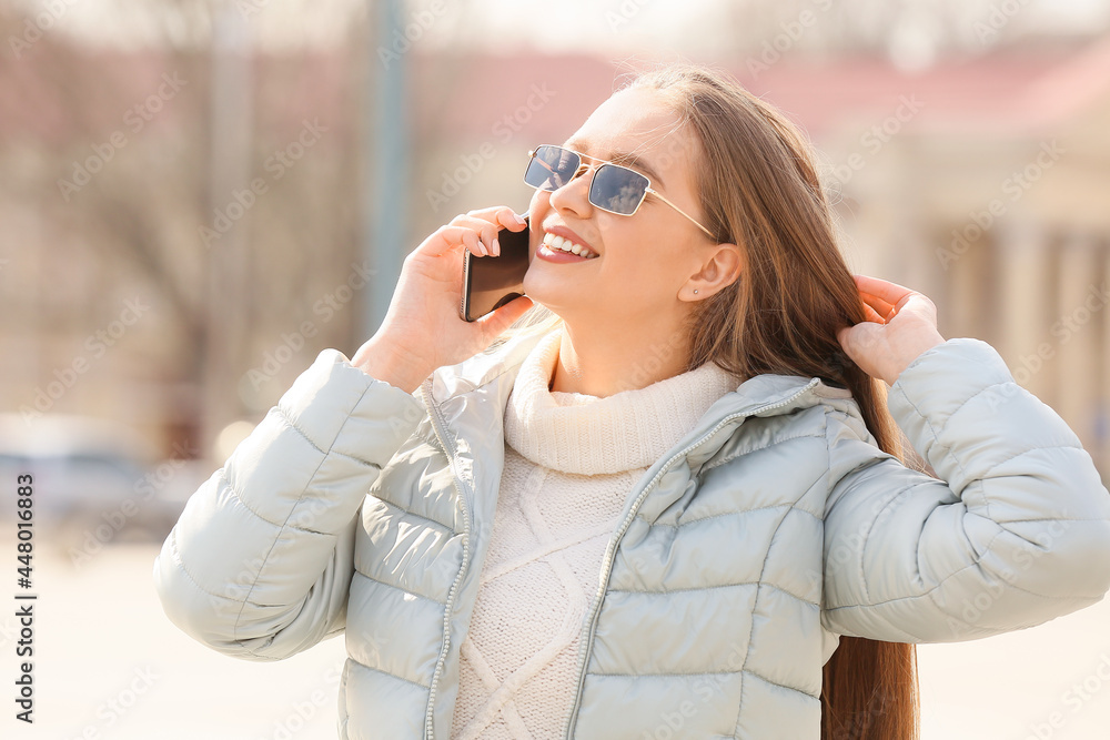 Wall mural Young woman talking by phone outdoors