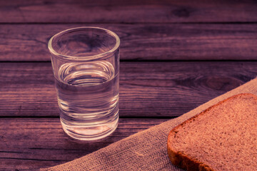 Shot of vodka with a piece of black bread and cloth cut on an old wooden table. Close up view