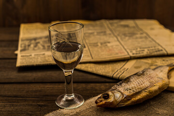 Glass of vodka with a stockfish and newspaper with canvas on an old wooden table. Angle view,...