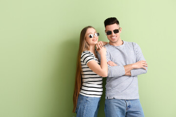 Young couple wearing stylish sunglasses on color background