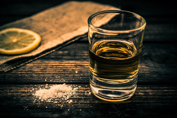 Glass of tequila with piece of cloth and a slice of lemon with salt on an old wooden table. Close up view, shallow depth of field