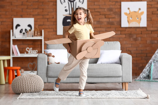 Little girl playing with cardboard airplane at home