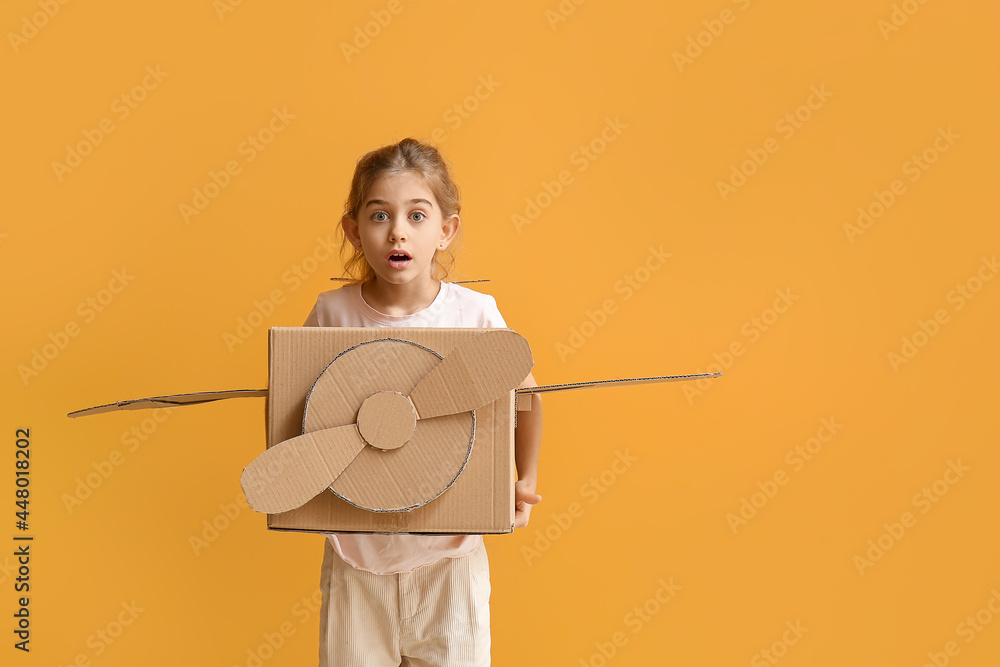 Wall mural Shocked little girl with cardboard airplane on color background