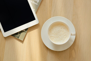 Cup of coffee and tablet computer on table in room