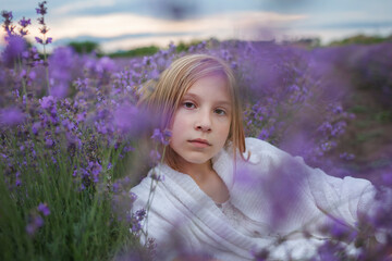 Teenage girl enjoys the scenery of lavender field. Dreamy teenager sitting among purple flowers. Calm landscape, escape to beauty of nature, summer lifestyle