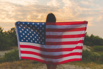 young woman posing with USA national flag standing outdoors at sunset.country, patriotism, independence day concept.