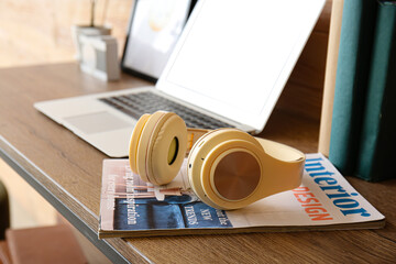 Modern headphones with magazine on table, closeup