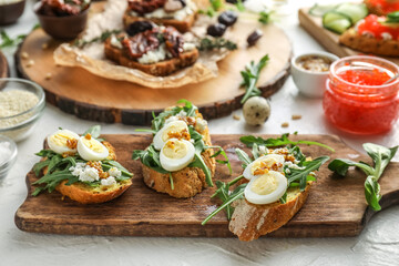 Fototapeta na wymiar Tasty bruschettas with cheese, eggs and arugula on light background